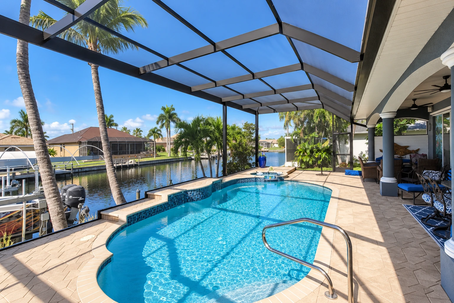 A screened pool enclosure with a dark metal frame shelters a swimming pool beside a canal and palm trees.